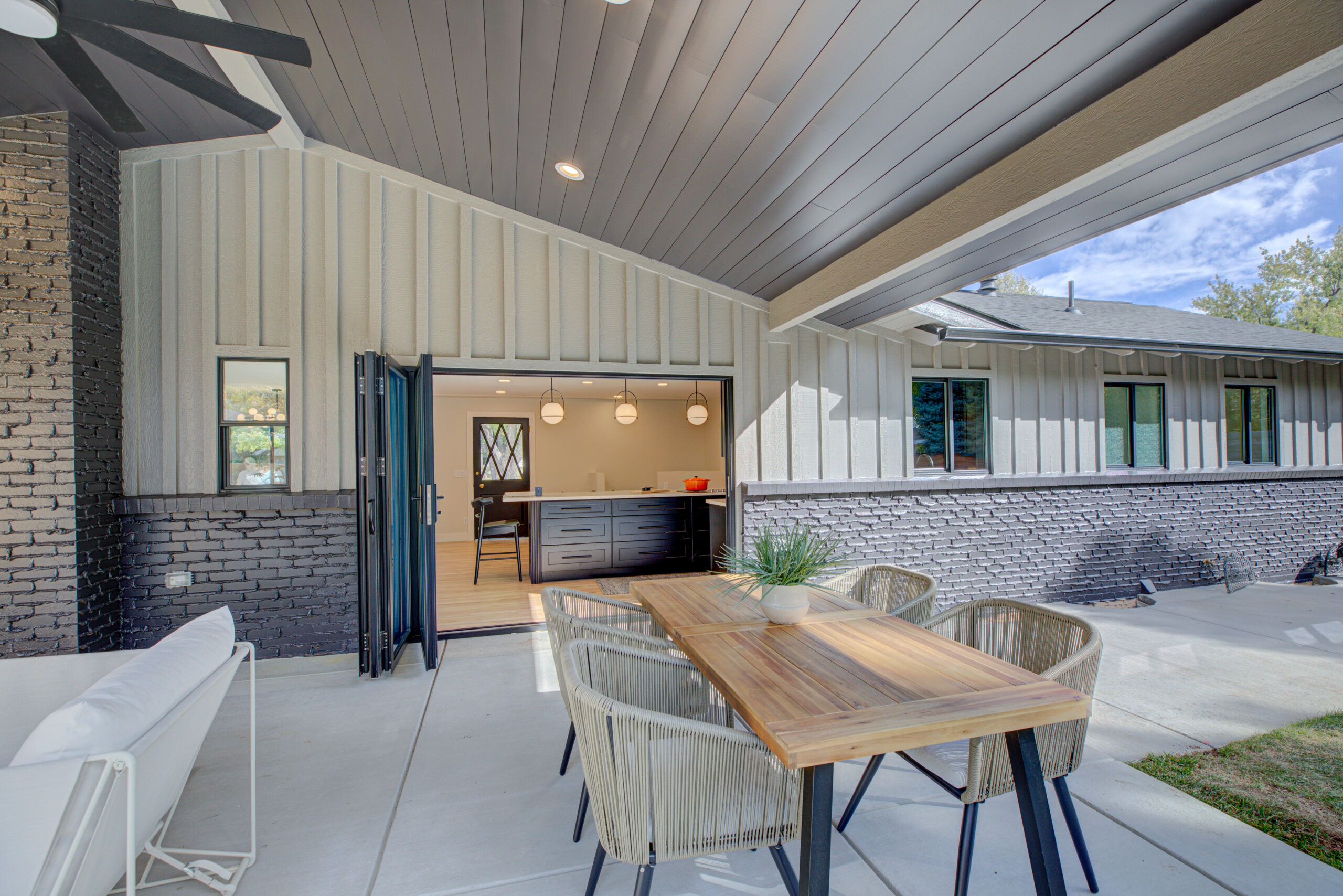 Spacious and modern covered patio area featuring a wooden dining table set and sleek black accents, with open sliding doors leading to a cozy interior, newly remodeled to reflect Denver's vibrant style.